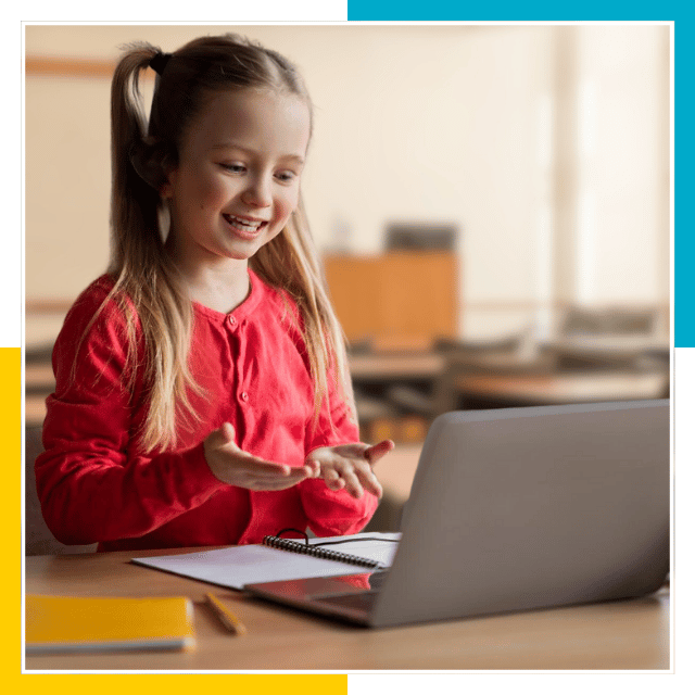 A young girl wearing a red sweater sits at a desk with a laptop, notebook, and pencil, participating in an online class in a classroom setting. Online sign language services at her fingertips.